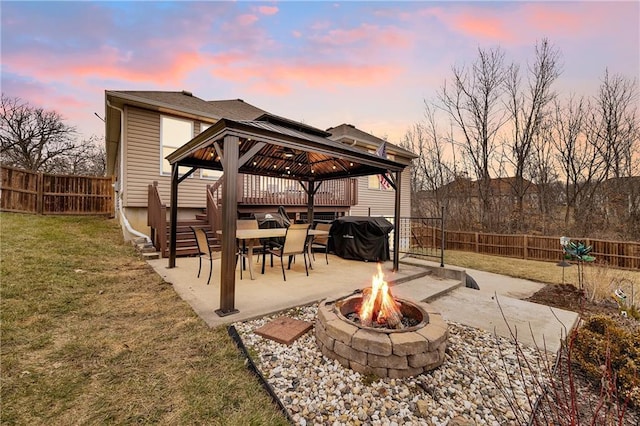 patio terrace at dusk with a lawn, area for grilling, a gazebo, and an outdoor fire pit