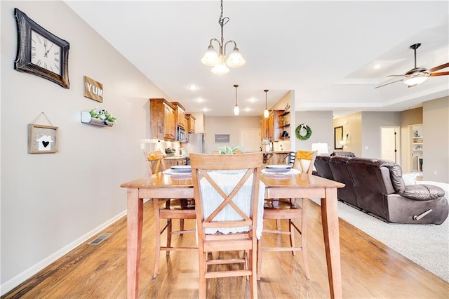 dining space with ceiling fan with notable chandelier and light hardwood / wood-style flooring