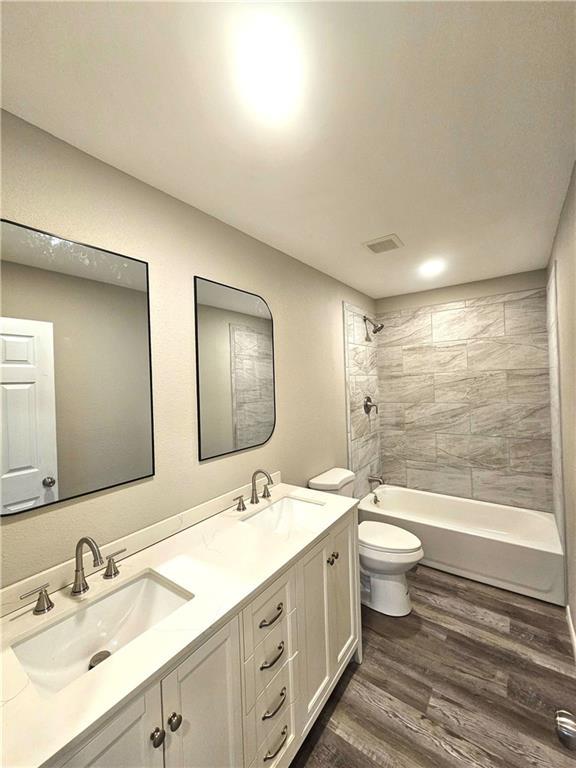 full bathroom featuring hardwood / wood-style flooring, vanity, tiled shower / bath combo, and toilet