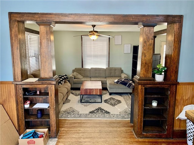 living room featuring wooden walls, decorative columns, ceiling fan, and light wood-type flooring