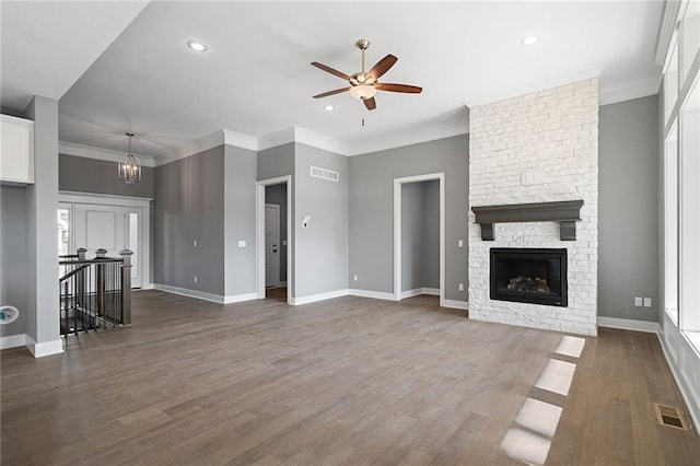 unfurnished living room featuring ornamental molding, dark hardwood / wood-style floors, ceiling fan with notable chandelier, and a stone fireplace