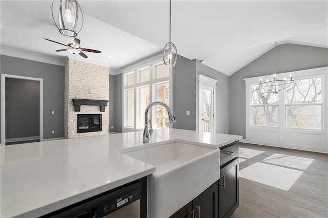 kitchen featuring a stone fireplace, decorative light fixtures, lofted ceiling, sink, and stainless steel dishwasher