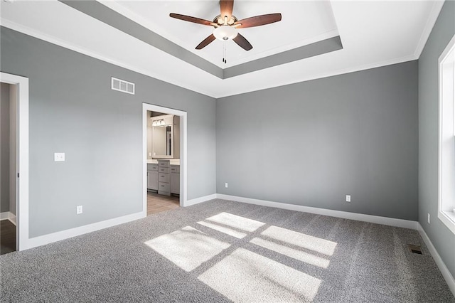 unfurnished bedroom with crown molding, ensuite bathroom, a tray ceiling, and light carpet