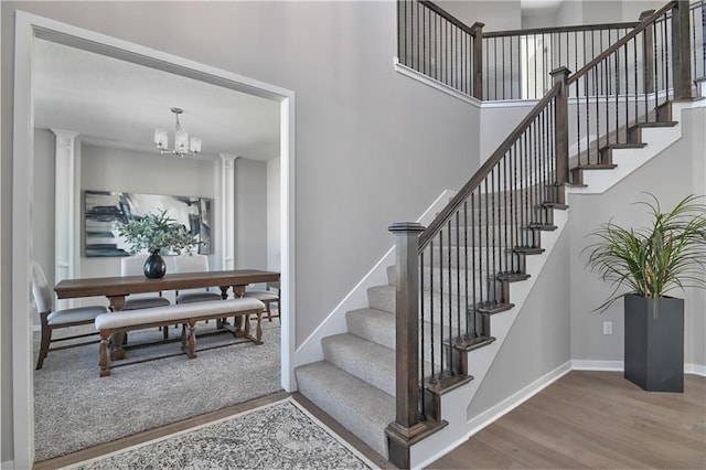 stairway featuring an inviting chandelier, a towering ceiling, hardwood / wood-style floors, and ornate columns