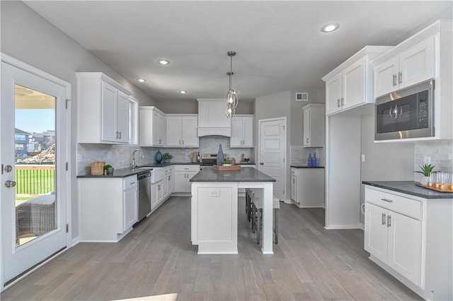 kitchen featuring pendant lighting, white cabinetry, stainless steel appliances, a center island, and light hardwood / wood-style floors