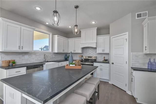 kitchen featuring appliances with stainless steel finishes, white cabinetry, hanging light fixtures, a center island, and dark hardwood / wood-style flooring