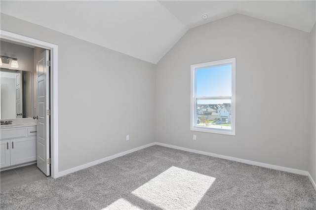 unfurnished bedroom with lofted ceiling, sink, light colored carpet, and ensuite bathroom