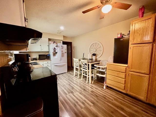 kitchen with a textured ceiling, white fridge with ice dispenser, ceiling fan, range hood, and hardwood / wood-style floors