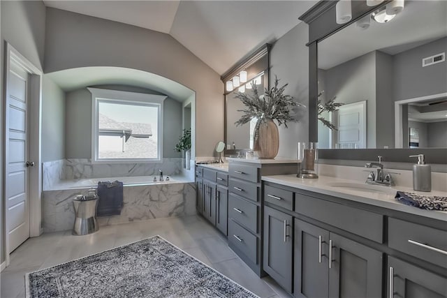 bathroom featuring tile patterned flooring, vanity, lofted ceiling, and a relaxing tiled tub