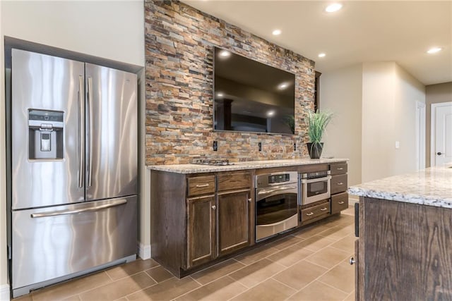 kitchen with appliances with stainless steel finishes, dark brown cabinetry, light stone counters, and light tile patterned floors