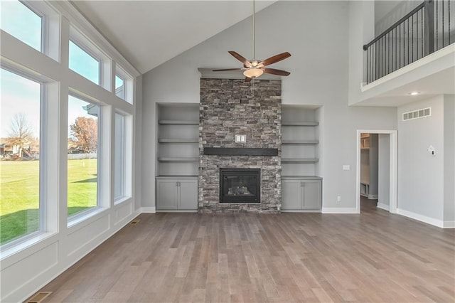 unfurnished living room with light hardwood / wood-style flooring, built in shelves, a wealth of natural light, and a stone fireplace