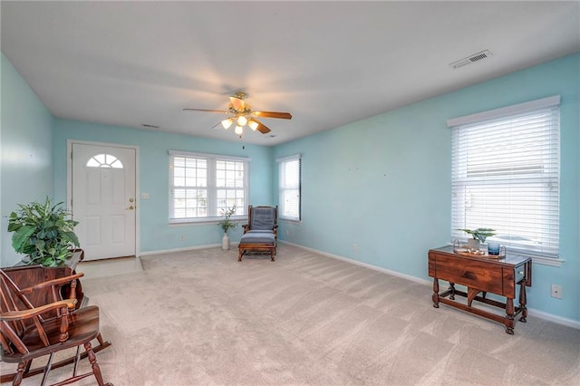 living area with baseboards, visible vents, ceiling fan, and light colored carpet