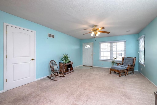 living area featuring a textured ceiling, visible vents, and light colored carpet