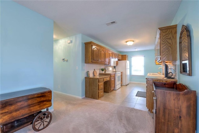 kitchen featuring light colored carpet, visible vents, brown cabinetry, a sink, and white appliances