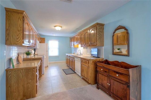 kitchen featuring brown cabinetry, decorative backsplash, dishwasher, light countertops, and a sink