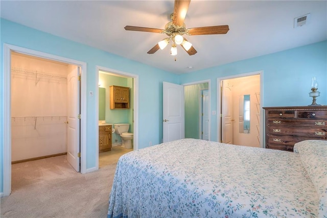 bedroom with a walk in closet, a closet, light colored carpet, visible vents, and baseboards