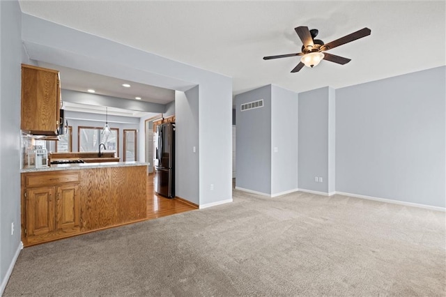 kitchen featuring pendant lighting, sink, fridge, light colored carpet, and kitchen peninsula