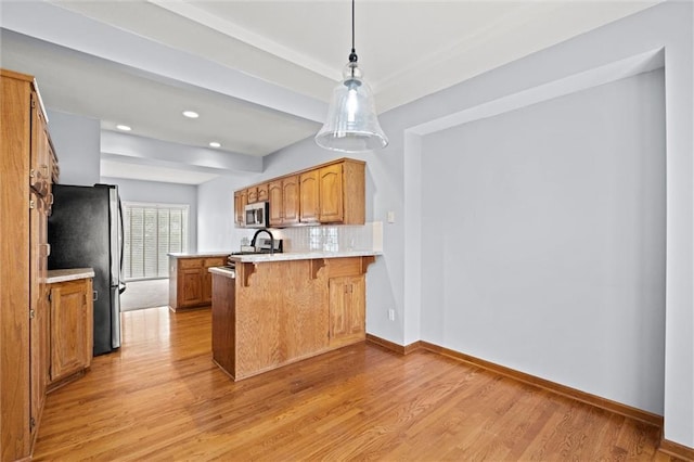 kitchen featuring light hardwood / wood-style flooring, appliances with stainless steel finishes, hanging light fixtures, a kitchen bar, and kitchen peninsula