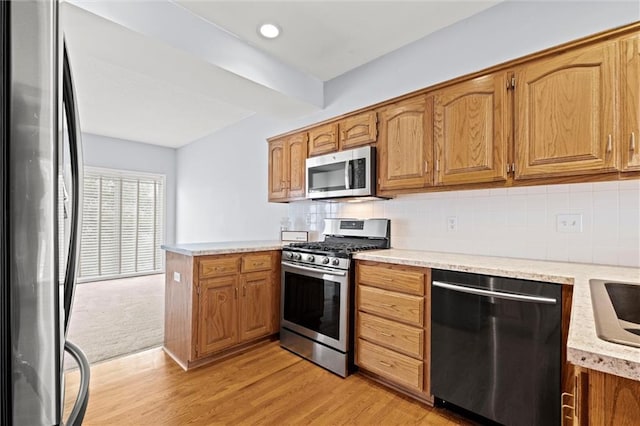 kitchen featuring backsplash, light wood-type flooring, kitchen peninsula, and appliances with stainless steel finishes