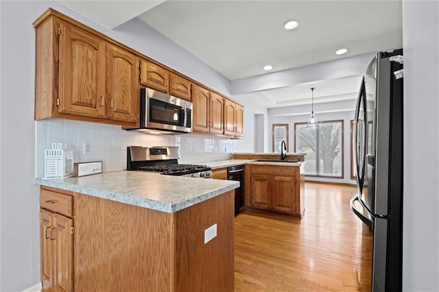 kitchen featuring decorative light fixtures, tasteful backsplash, kitchen peninsula, stainless steel appliances, and light wood-type flooring