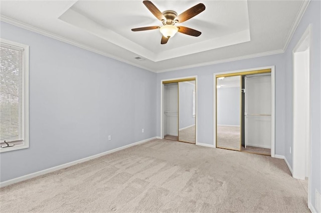 unfurnished bedroom with multiple closets, ornamental molding, light colored carpet, and a tray ceiling