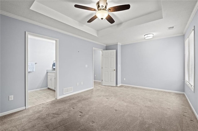 unfurnished bedroom with light carpet, crown molding, ensuite bath, and a raised ceiling