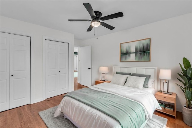 bedroom with multiple closets, hardwood / wood-style flooring, and ceiling fan