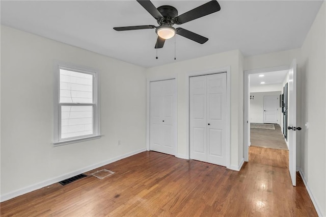 unfurnished bedroom featuring ceiling fan, hardwood / wood-style flooring, and multiple closets