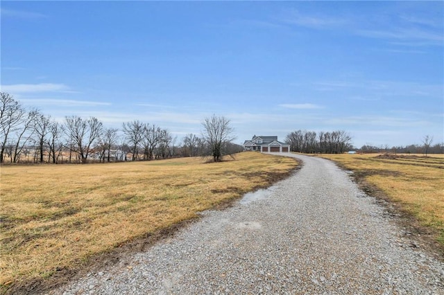 view of street with gravel driveway and a rural view