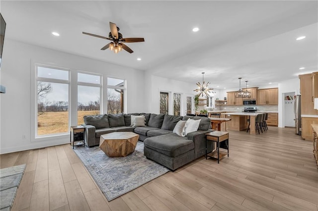 living room with ceiling fan with notable chandelier, light wood-type flooring, and recessed lighting