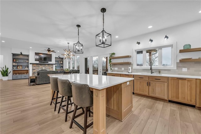 kitchen with light wood-style floors, open shelves, a sink, and a stone fireplace