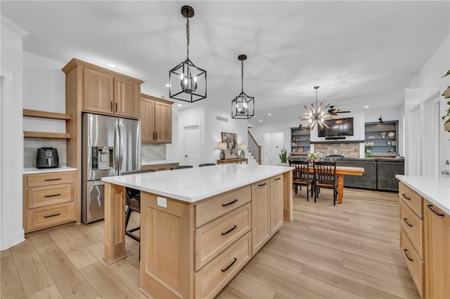 kitchen with stainless steel fridge, a kitchen island, light countertops, light wood-type flooring, and light brown cabinets