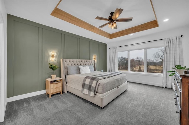 carpeted bedroom with a raised ceiling, a decorative wall, baseboards, and ceiling fan