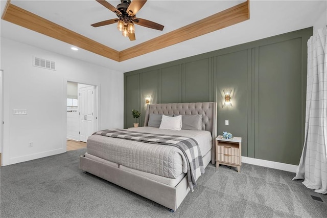 bedroom with carpet floors, a raised ceiling, visible vents, and a decorative wall