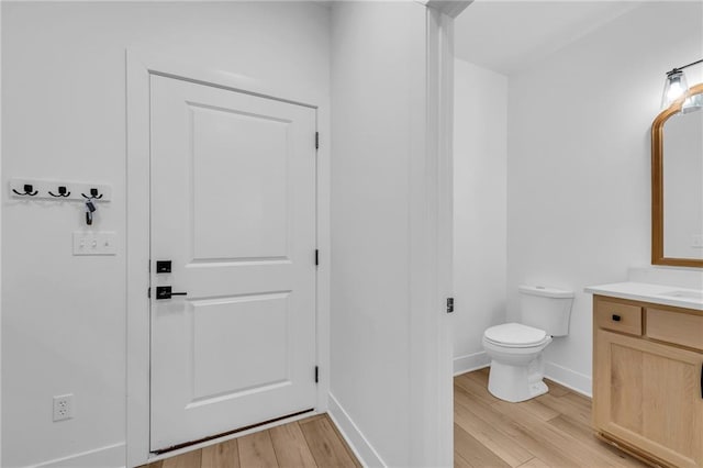 bathroom with toilet, wood finished floors, vanity, and baseboards