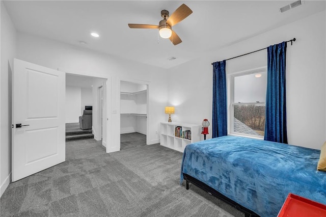 carpeted bedroom with ceiling fan, a spacious closet, visible vents, and baseboards