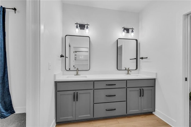 bathroom featuring double vanity, wood finished floors, a sink, and baseboards