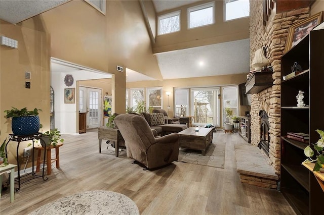 living room featuring a stone fireplace, a towering ceiling, and light wood-type flooring