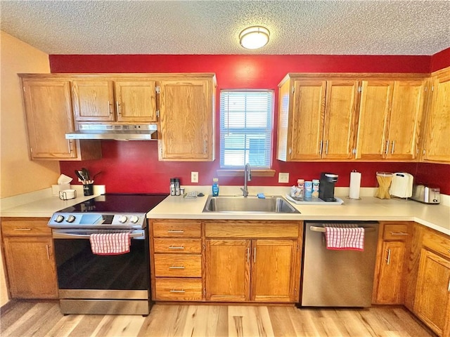 kitchen featuring appliances with stainless steel finishes, sink, a textured ceiling, and light wood-type flooring