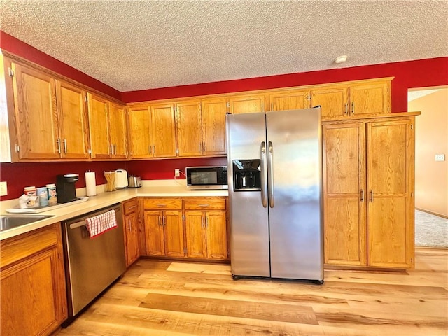 kitchen featuring stainless steel appliances, light hardwood / wood-style floors, and a textured ceiling