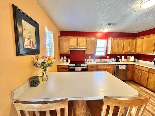 kitchen featuring stainless steel appliances, sink, a textured ceiling, and light hardwood / wood-style flooring