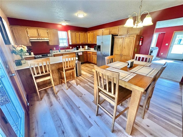 dining room with an inviting chandelier, sink, a textured ceiling, and light wood-type flooring