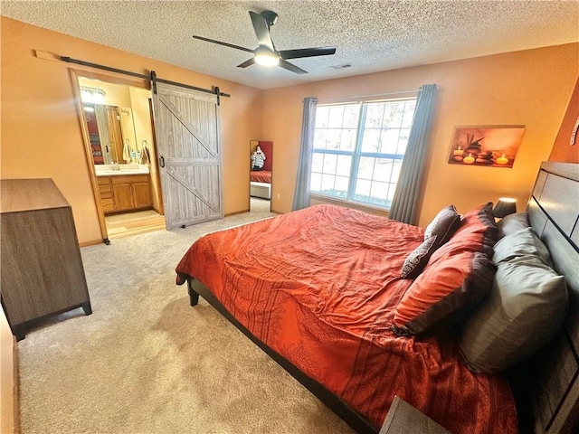 carpeted bedroom featuring sink, ensuite bath, a textured ceiling, ceiling fan, and a barn door