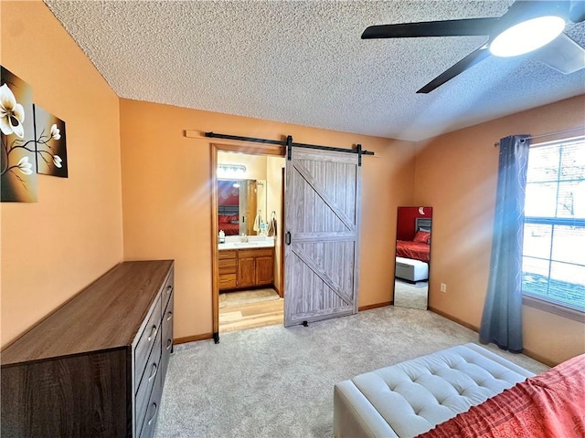 bedroom featuring ceiling fan, ensuite bathroom, a textured ceiling, light colored carpet, and a barn door