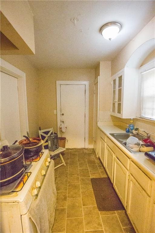 kitchen featuring light countertops, white gas range, a sink, and glass insert cabinets