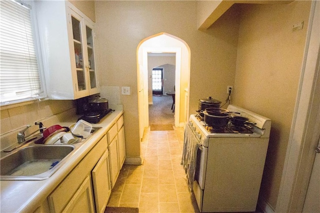 kitchen featuring white range with gas cooktop, arched walkways, decorative backsplash, light countertops, and a sink