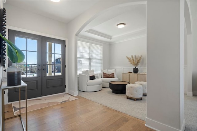 foyer with arched walkways, a wainscoted wall, wood finished floors, a tray ceiling, and french doors