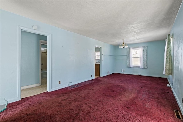 carpeted empty room featuring a notable chandelier and a textured ceiling