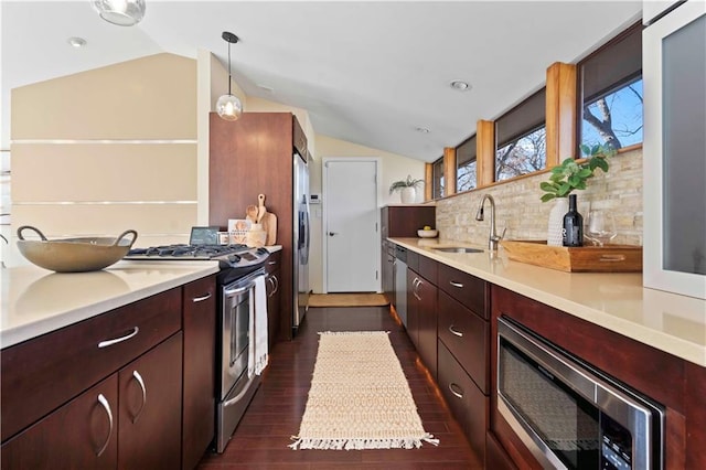 kitchen with lofted ceiling, sink, hanging light fixtures, appliances with stainless steel finishes, and decorative backsplash