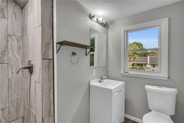 bathroom featuring vanity, tiled shower, a textured ceiling, and toilet